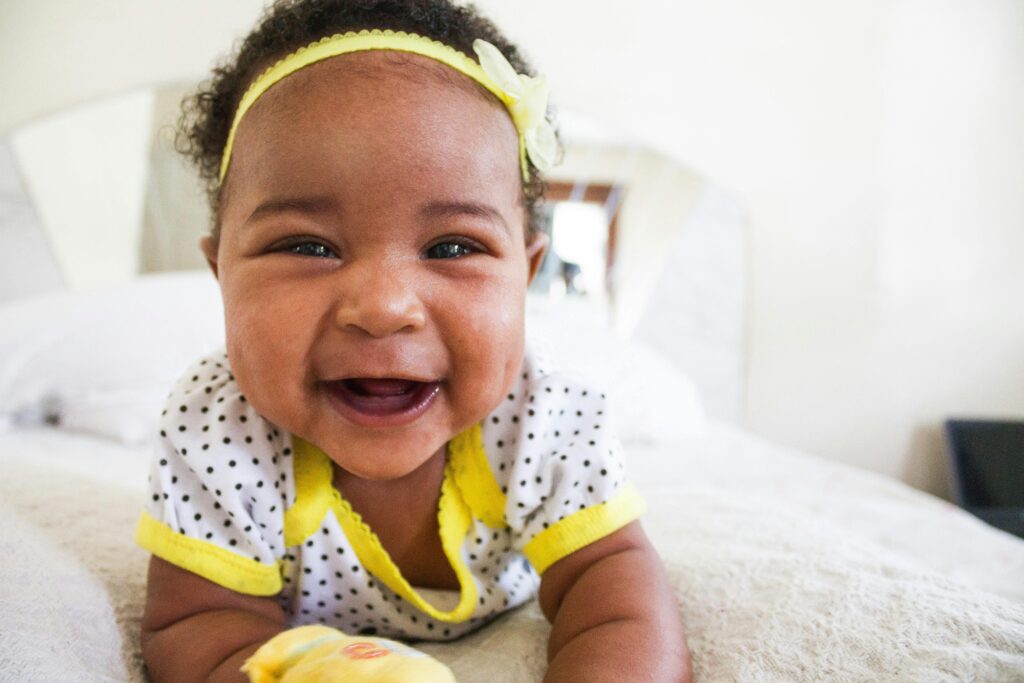 pexels-photo-774910-774910 Cheerful baby girl in a polka dot outfit with a big smile on a bed indoors.
