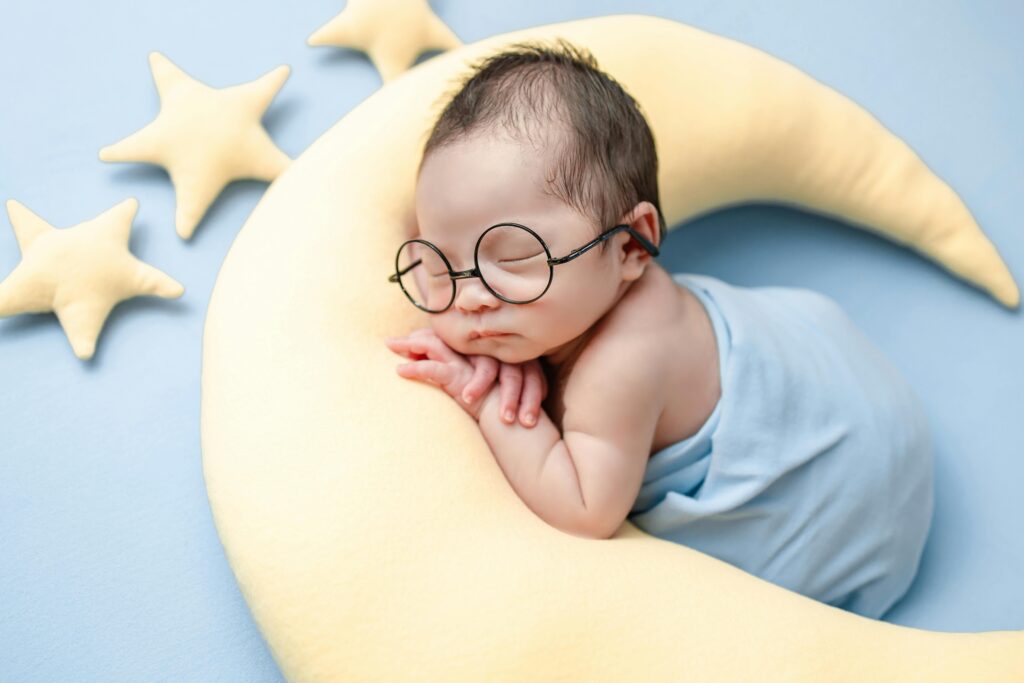 pexels-photo-8794620-8794620 Charming image of a newborn baby sleeping on a crescent moon pillow, wrapped in a blue blanket.